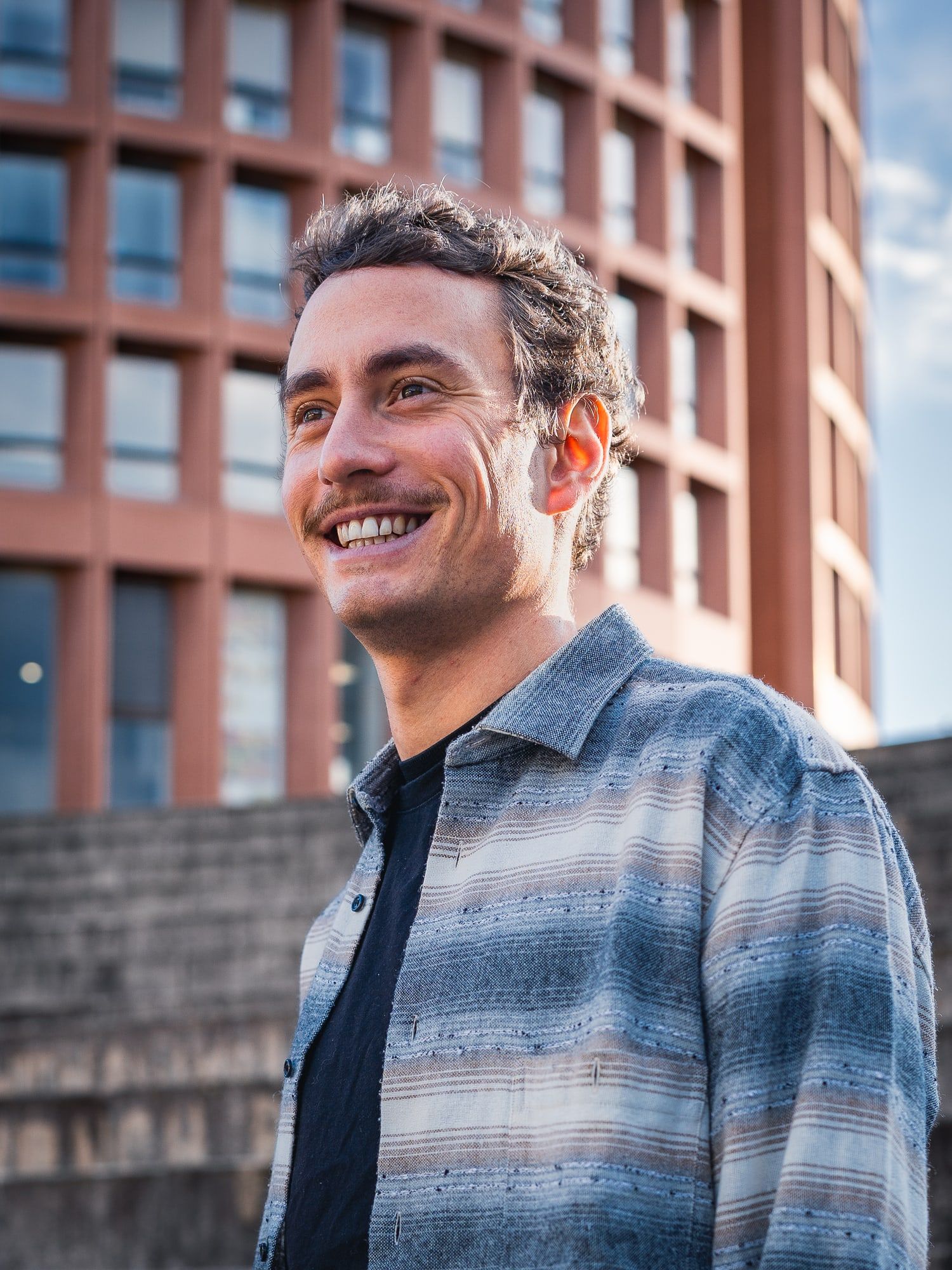 Thomas, souriant, devant une tour de briques rouges